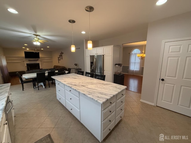 kitchen with light tile patterned floors, hanging light fixtures, stainless steel refrigerator with ice dispenser, white cabinets, and a kitchen island