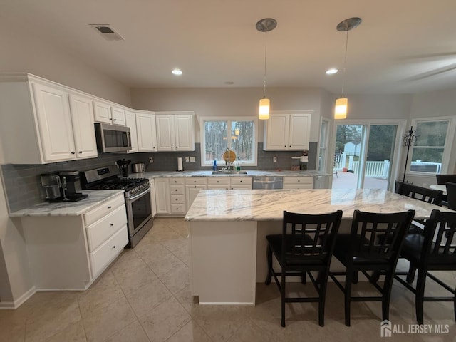 kitchen with light stone counters, stainless steel appliances, white cabinets, and a kitchen island