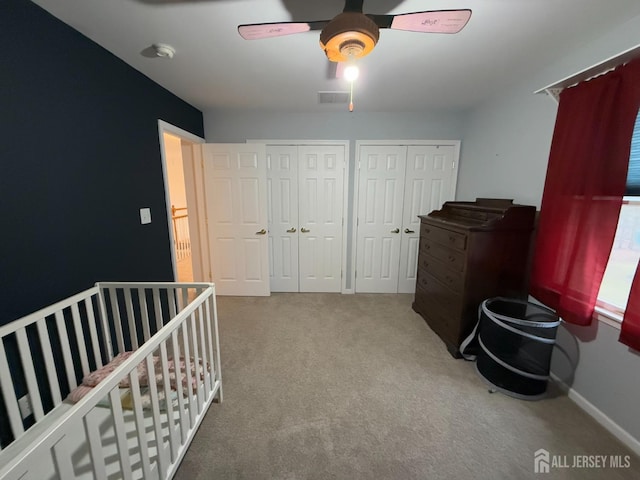 carpeted bedroom with multiple closets, ceiling fan, baseboards, and a crib