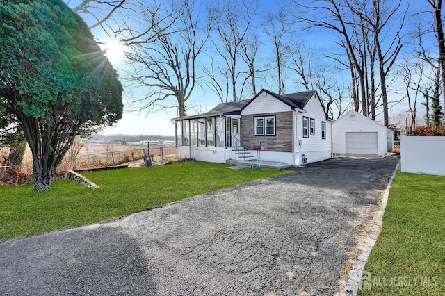 view of front of property featuring an outbuilding, a garage, a front yard, and a sunroom