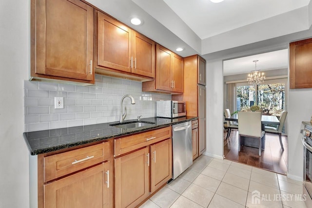 kitchen with dark stone counters, sink, light tile patterned floors, a notable chandelier, and stainless steel appliances