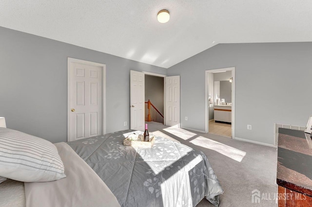 bedroom with ensuite bathroom, light colored carpet, and lofted ceiling