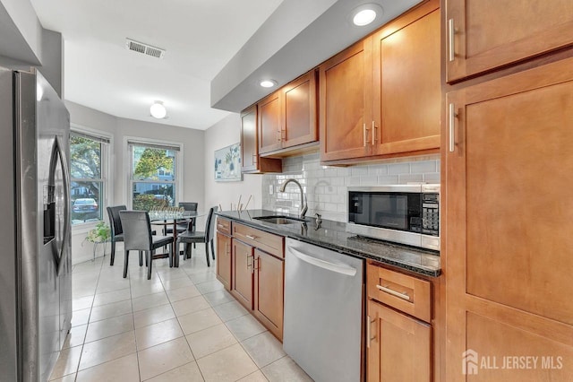 kitchen featuring sink, dark stone countertops, decorative backsplash, light tile patterned floors, and appliances with stainless steel finishes