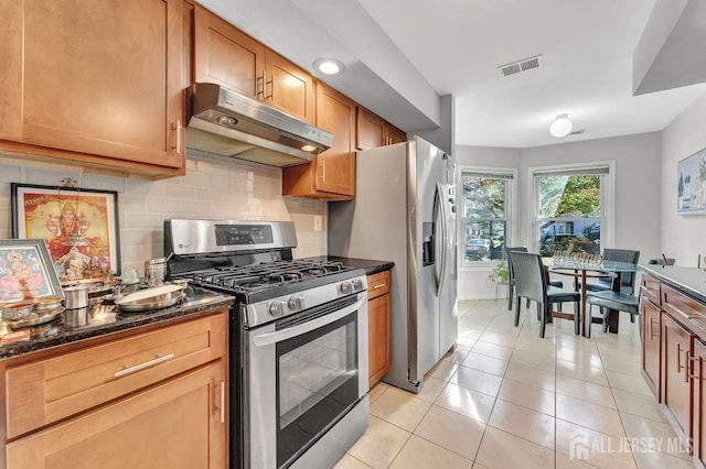 kitchen with light tile patterned floors, stainless steel appliances, dark stone counters, and tasteful backsplash