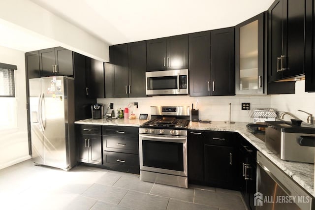 kitchen with light stone counters, stainless steel appliances, and dark cabinets