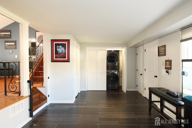 entryway featuring stacked washer and clothes dryer, stairs, baseboards, and dark wood-style floors