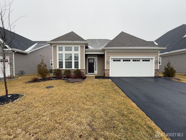 view of front of home featuring an attached garage, a shingled roof, a front lawn, stone siding, and aphalt driveway