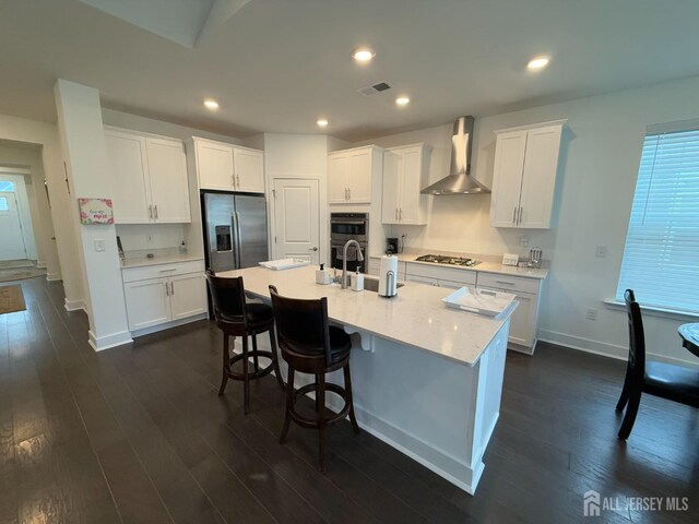 kitchen featuring wall chimney exhaust hood, white cabinetry, appliances with stainless steel finishes, dark hardwood / wood-style floors, and a kitchen island with sink