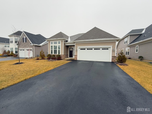 ranch-style home featuring a front yard, driveway, an attached garage, a shingled roof, and stone siding