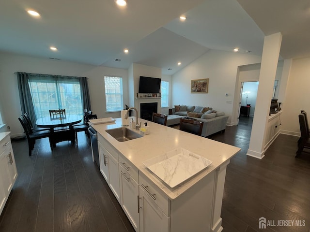 kitchen with a sink, vaulted ceiling, a fireplace, white cabinets, and dark wood-style flooring