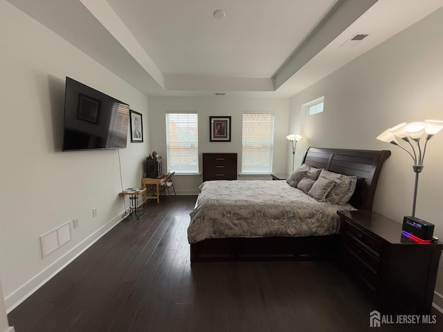 bedroom with a tray ceiling, multiple windows, visible vents, and dark wood-style floors