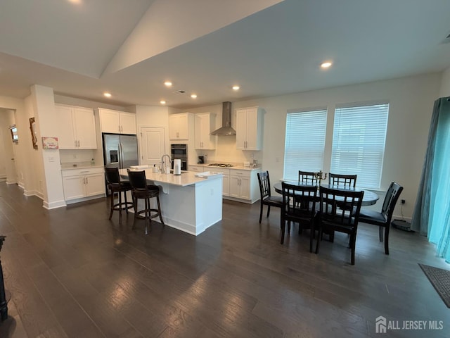 kitchen featuring dark wood-style flooring, stainless steel appliances, light countertops, white cabinets, and wall chimney exhaust hood