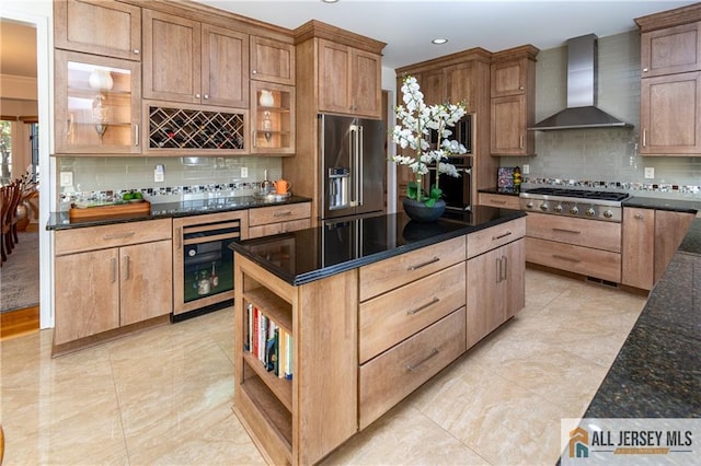 kitchen featuring wall chimney range hood, appliances with stainless steel finishes, tasteful backsplash, beverage cooler, and dark stone counters