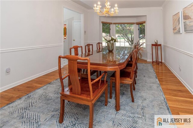 dining room with an inviting chandelier, baseboards, crown molding, and wood finished floors