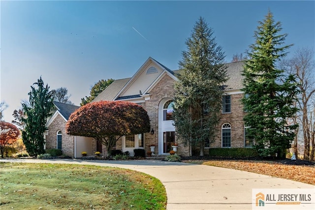 view of front facade with concrete driveway, brick siding, and a front yard