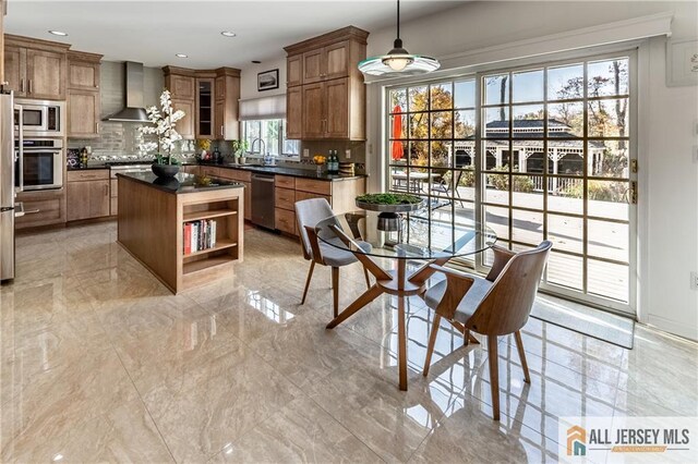 kitchen with decorative light fixtures, stainless steel appliances, wall chimney exhaust hood, dark countertops, and glass insert cabinets