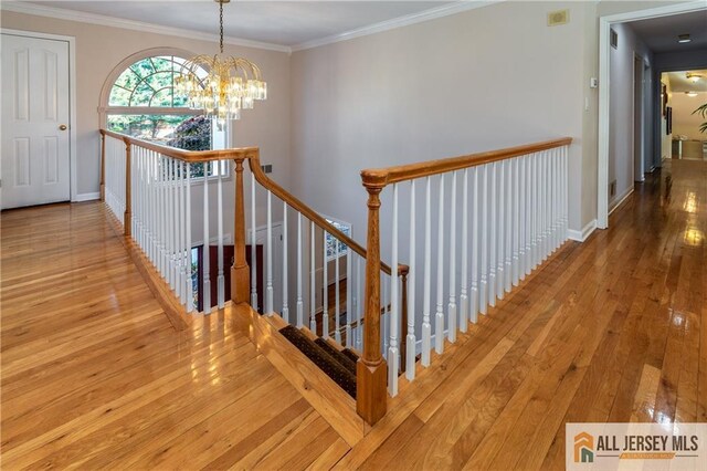 hallway with ornamental molding, hardwood / wood-style flooring, an upstairs landing, and an inviting chandelier