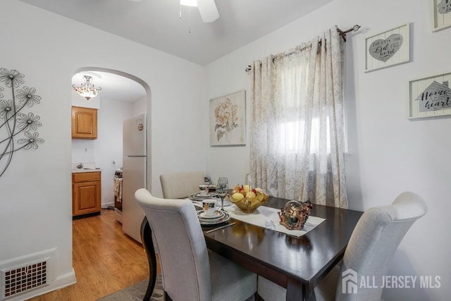 dining space with ceiling fan with notable chandelier and light hardwood / wood-style flooring