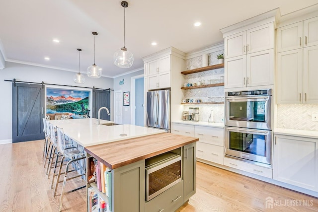 kitchen with butcher block counters, appliances with stainless steel finishes, a barn door, a sink, and open shelves