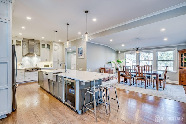 kitchen with light wood-style flooring, wall chimney range hood, ornamental molding, and beverage cooler