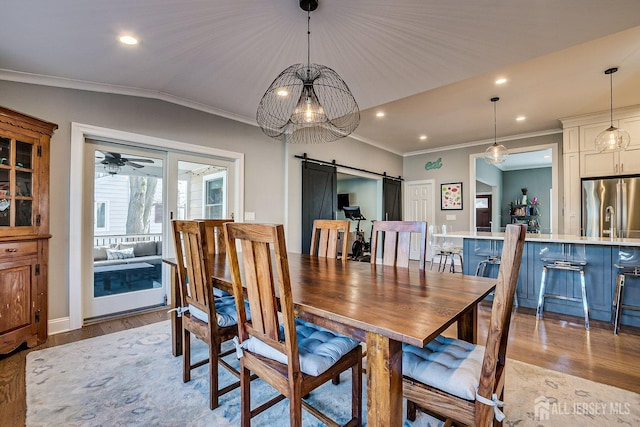 dining space featuring light wood-style floors, lofted ceiling, a barn door, and ornamental molding