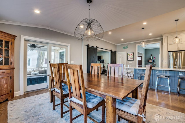 dining area with ornamental molding, a barn door, lofted ceiling, and light wood-type flooring