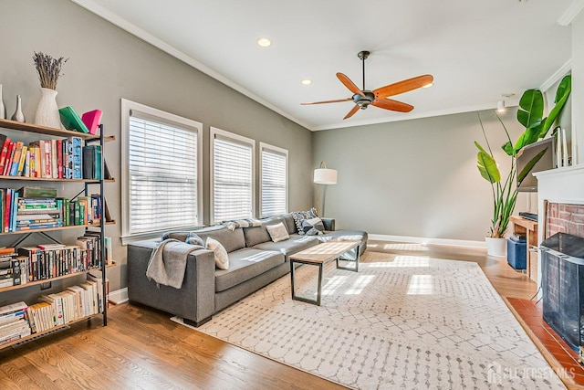 living room with crown molding, a brick fireplace, wood finished floors, and baseboards