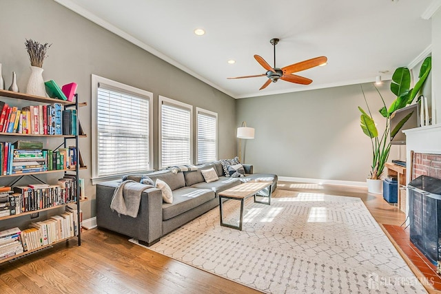 living room featuring wood finished floors, ornamental molding, baseboards, and ceiling fan