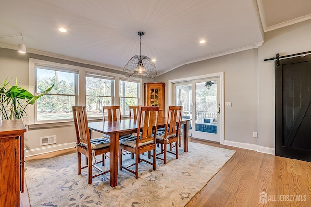 dining room with visible vents, light wood-style flooring, a barn door, crown molding, and baseboards