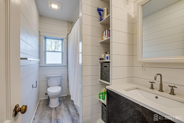 full bath with toilet, wood finished floors, vanity, and wood walls