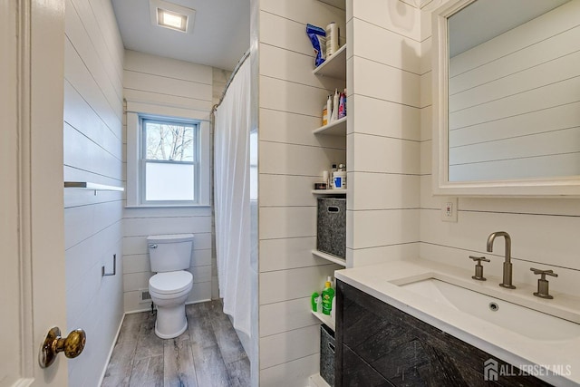 bathroom featuring vanity, toilet, wooden walls, and wood finished floors