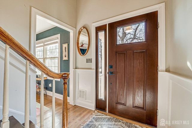 entryway featuring wainscoting, visible vents, stairs, and light wood-type flooring