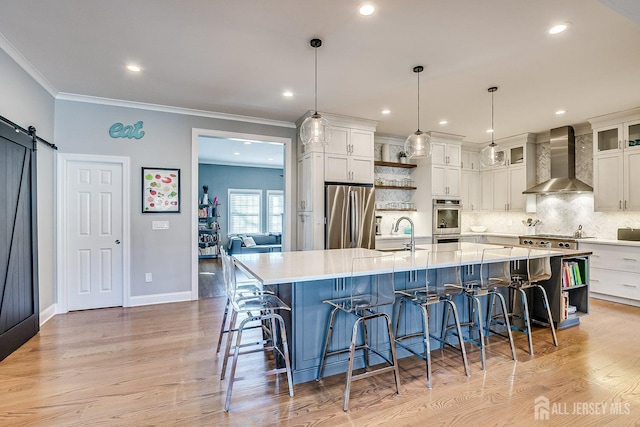 kitchen with wall chimney range hood, light wood finished floors, ornamental molding, and stainless steel fridge