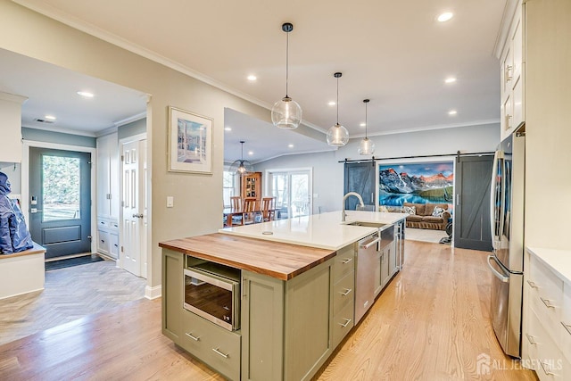 kitchen featuring butcher block counters, a barn door, ornamental molding, stainless steel appliances, and a sink