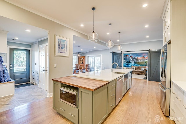 kitchen with recessed lighting, butcher block counters, appliances with stainless steel finishes, an island with sink, and a sink
