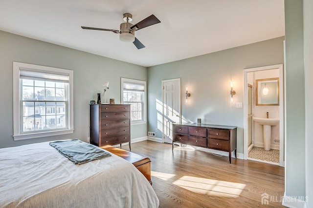 bedroom with wood finished floors, baseboards, ensuite bath, ceiling fan, and a sink