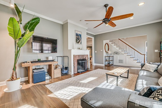 living area featuring a brick fireplace, baseboards, stairs, ornamental molding, and wood finished floors