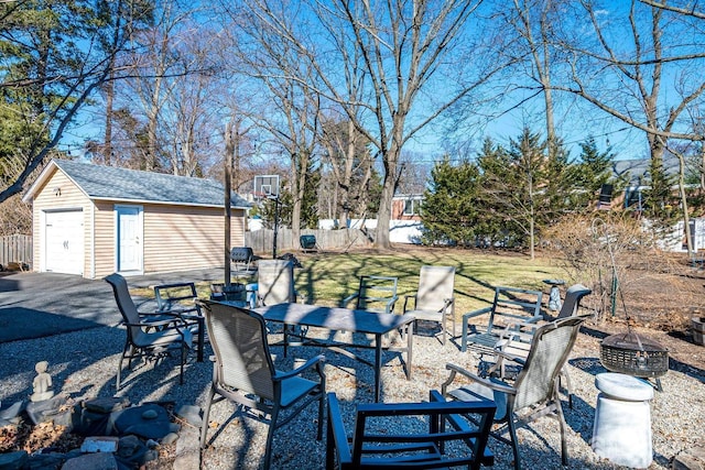 view of patio / terrace featuring fence, a detached garage, an outdoor fire pit, outdoor dining area, and an outdoor structure