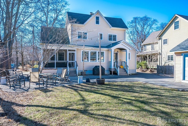 rear view of property featuring a patio, a shingled roof, a yard, and a sunroom