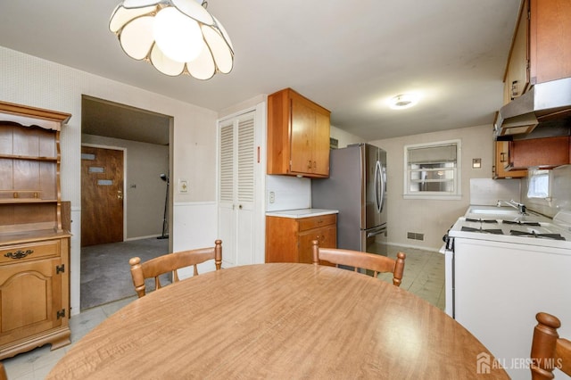 kitchen featuring freestanding refrigerator, brown cabinets, a sink, white range with gas stovetop, and visible vents