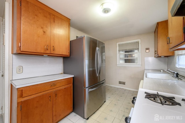 kitchen with brown cabinets, a sink, visible vents, light countertops, and freestanding refrigerator