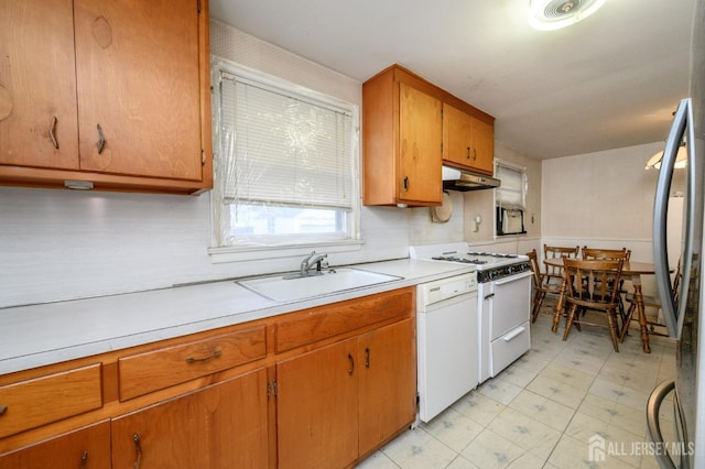 kitchen with white appliances, under cabinet range hood, light countertops, brown cabinets, and a sink
