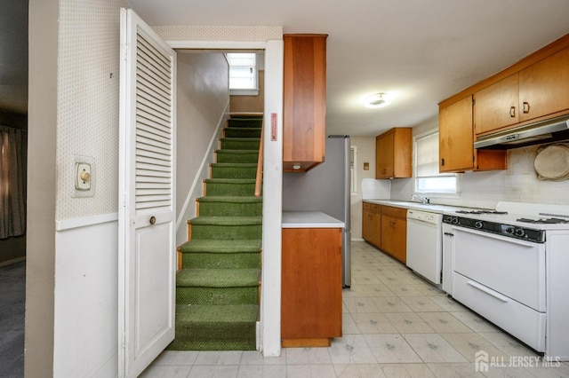 kitchen featuring under cabinet range hood, white appliances, brown cabinetry, light countertops, and light floors