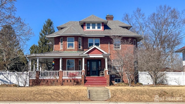 view of front facade featuring a porch, brick siding, fence, roof with shingles, and a chimney