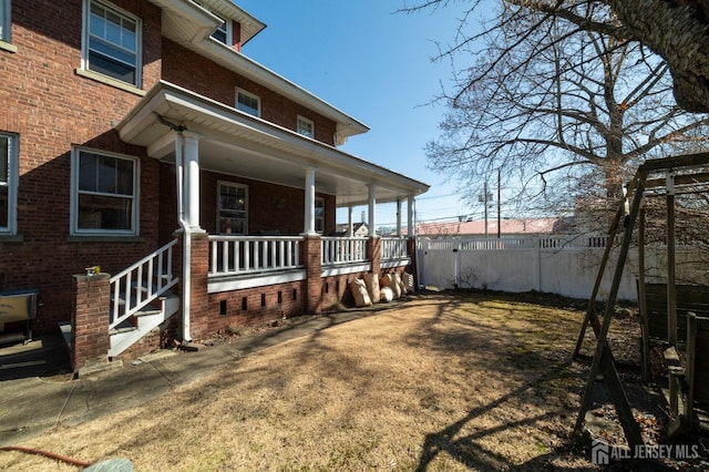 exterior space featuring covered porch, brick siding, and fence