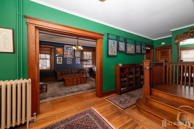 interior space with a chandelier, wood finished floors, baseboards, ornamental molding, and radiator heating unit