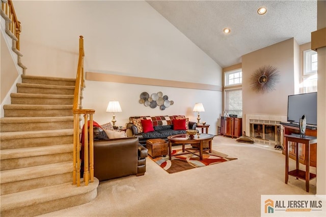 living area with a tiled fireplace, stairs, a textured ceiling, carpet floors, and high vaulted ceiling