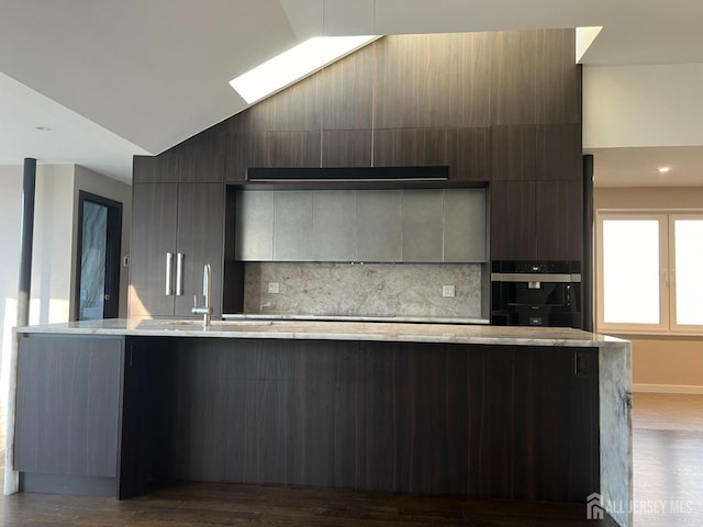 kitchen with vaulted ceiling with skylight, sink, oven, decorative backsplash, and hardwood / wood-style flooring