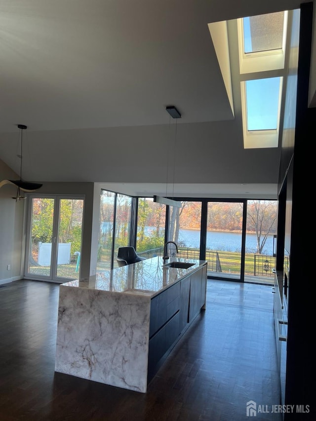 kitchen with sink, a water view, light stone countertops, decorative light fixtures, and a large island with sink