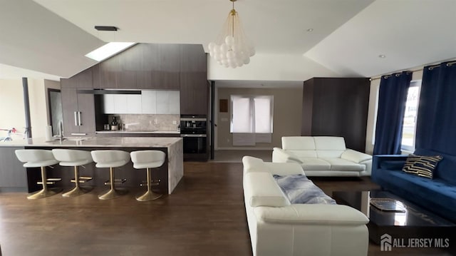 living room with an inviting chandelier, sink, dark wood-type flooring, and lofted ceiling with skylight